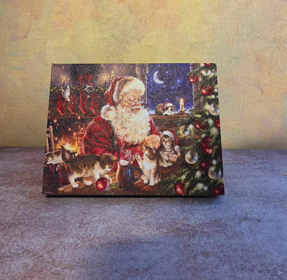 Santa’s Furry Friends light-up Christmas tabletop canvas featuring Santa with cats, a decorated Christmas tree, fireplace, stockings, and cozy holiday details.