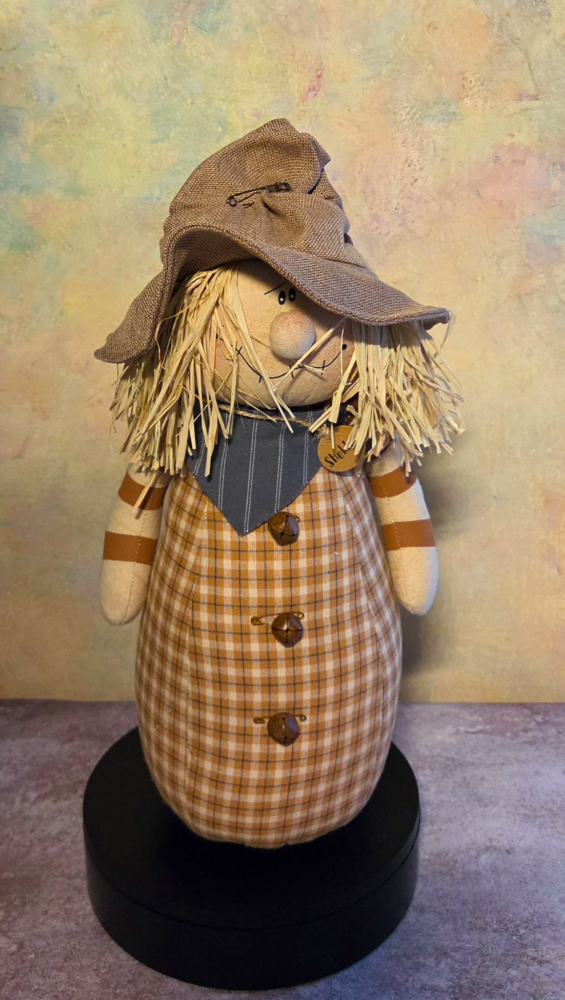 Front view of Sheldon scarecrow soft sculpture with a floppy hat, straw hair, plaid body, striped arms, scarf, and rustic buttons.