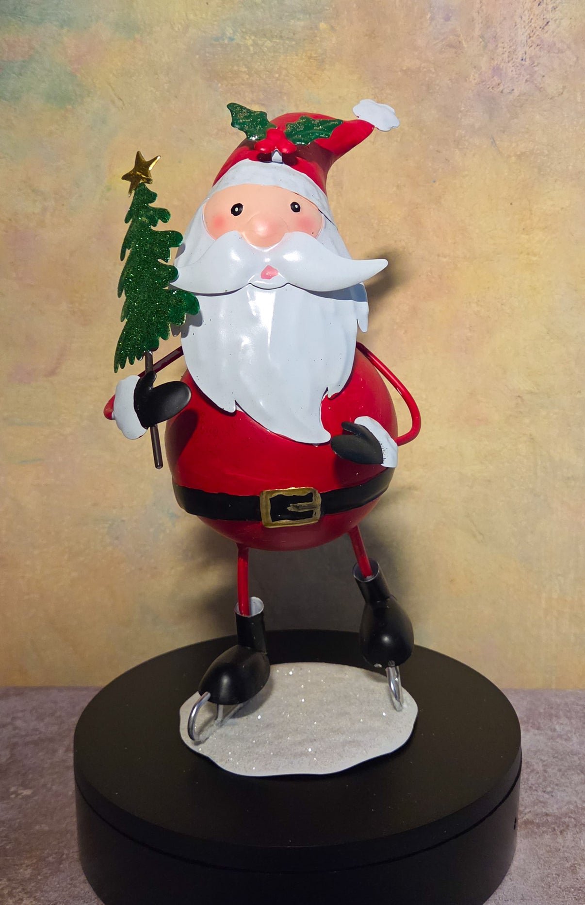 Front view of a tin Christmas snowman figurine ice skating while holding a large glittery white snowflake.