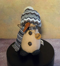 Front view of Slush snowman soft sculpture with a striped knit hat and scarf, long carrot nose, jingle bell buttons, and wooden name tag.