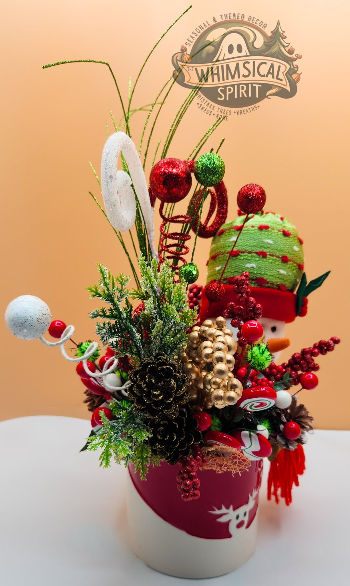 Decorative Christmas arrangement with a snowman theme on a beige background, featuring the 'Whimsical Spirit' brand.