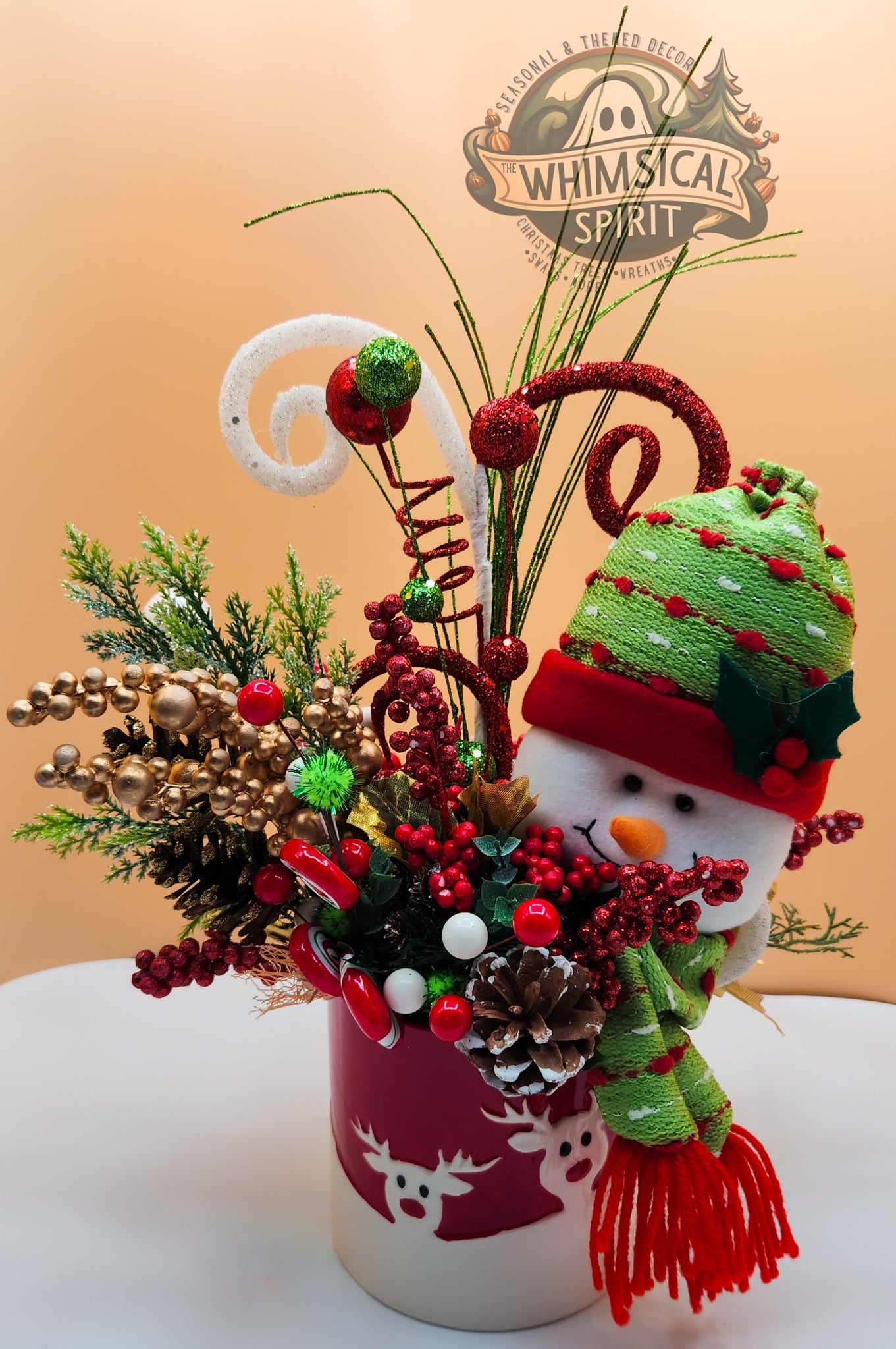 Decorative arrangement with a snowman figure, candy canes, and pinecones on a beige background with 'Whimsical Spirit' branding.