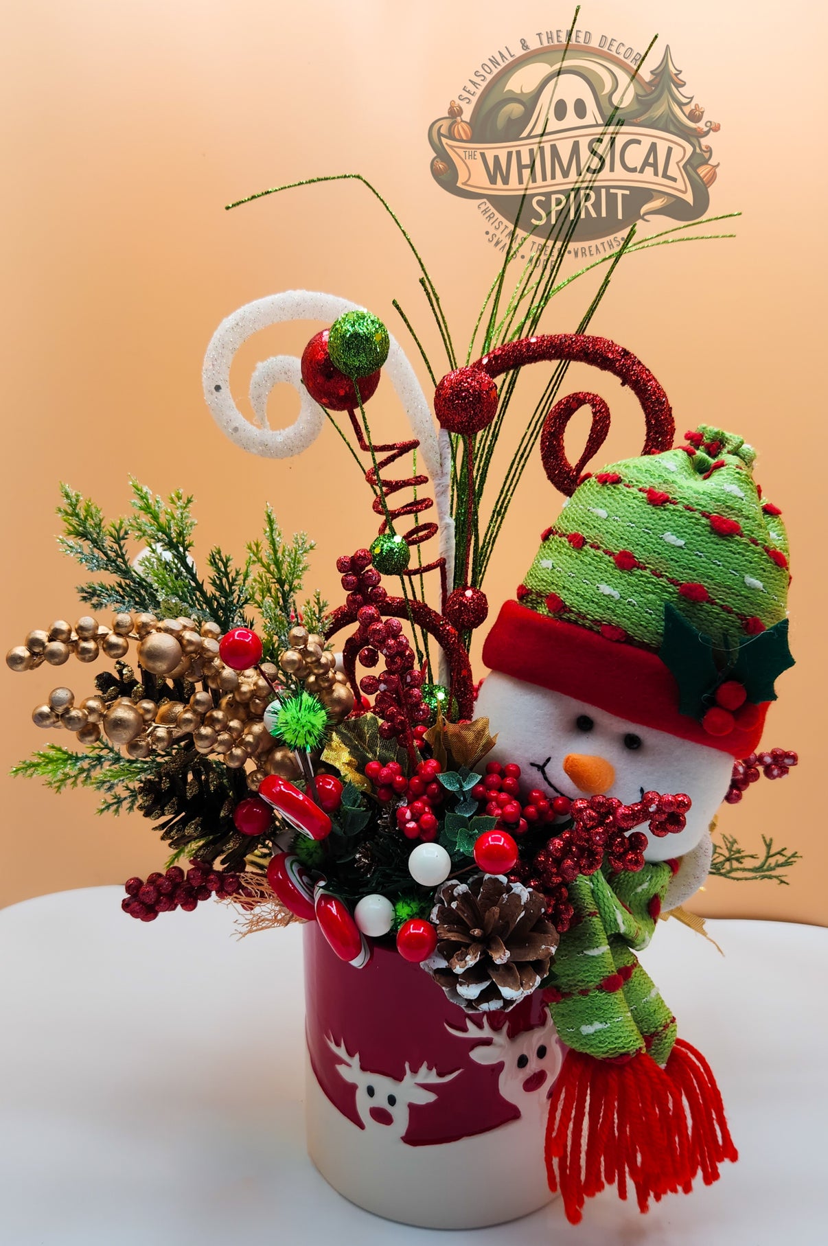 Decorative arrangement with a snowman figure, candy canes, and pinecones on a beige background with 'Whimsical Spirit' branding.