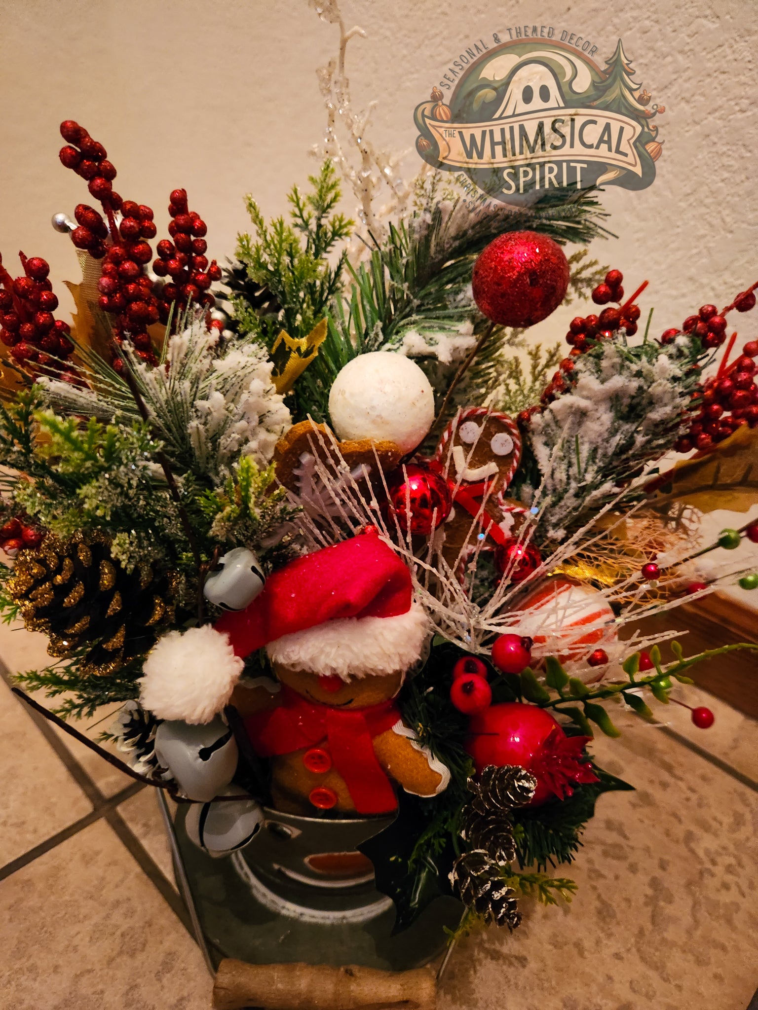 Decorative Christmas arrangement with gingerbread man, pine cones, and red berries on a neutral background.