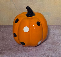 Glossy orange decorative pumpkin with scattered black and white polka dots and a curved black stem.