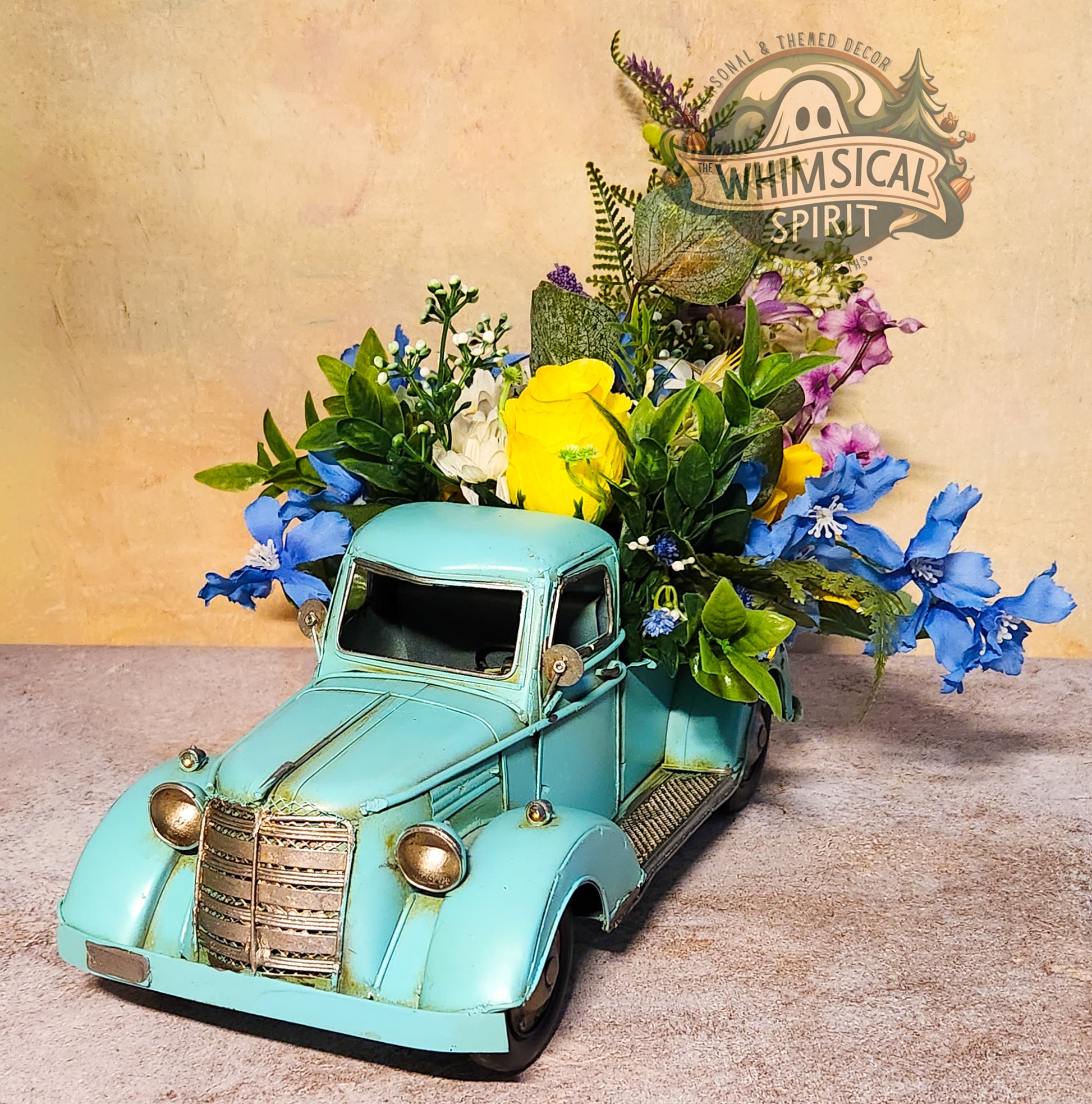 Decorative turquoise truck with flowers on a textured surface, featuring 'Whimsical Spirit' branding.