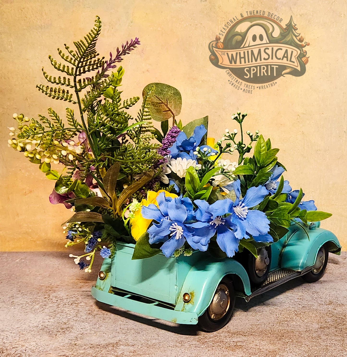 Decorative arrangement of flowers in a miniature teal car with 'Whimsical Spirit' branding.