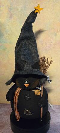 Front view of Stormy black cat soft sculpture with an extra-tall witch hat, orange plaid scarf, broom, rustic buttons, and wooden name tag.