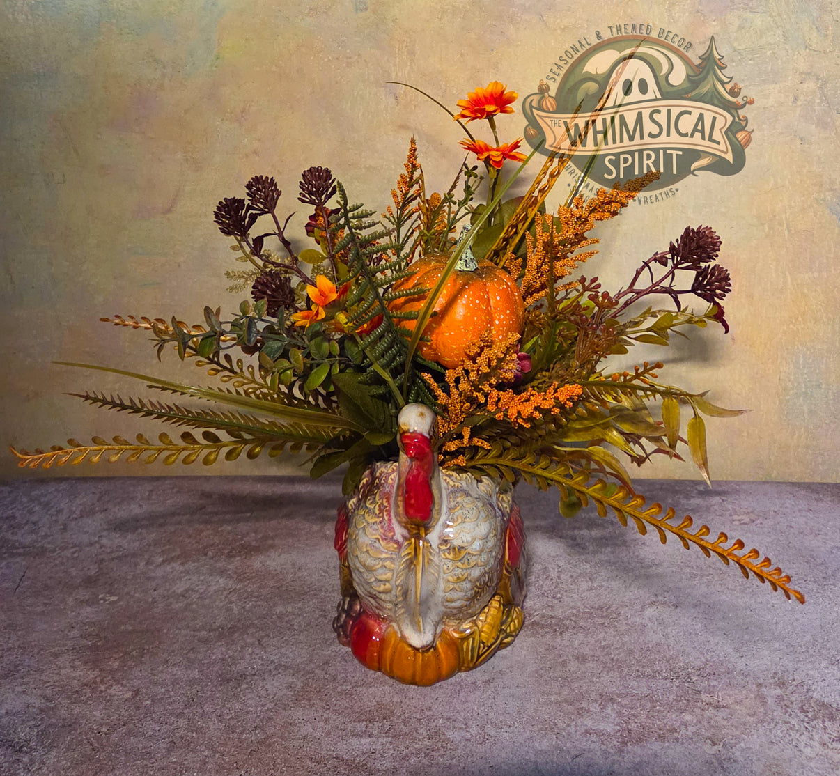 Handmade Thanksgiving centerpiece with a ceramic turkey, orange pumpkin, autumn florals, and trailing foliage.