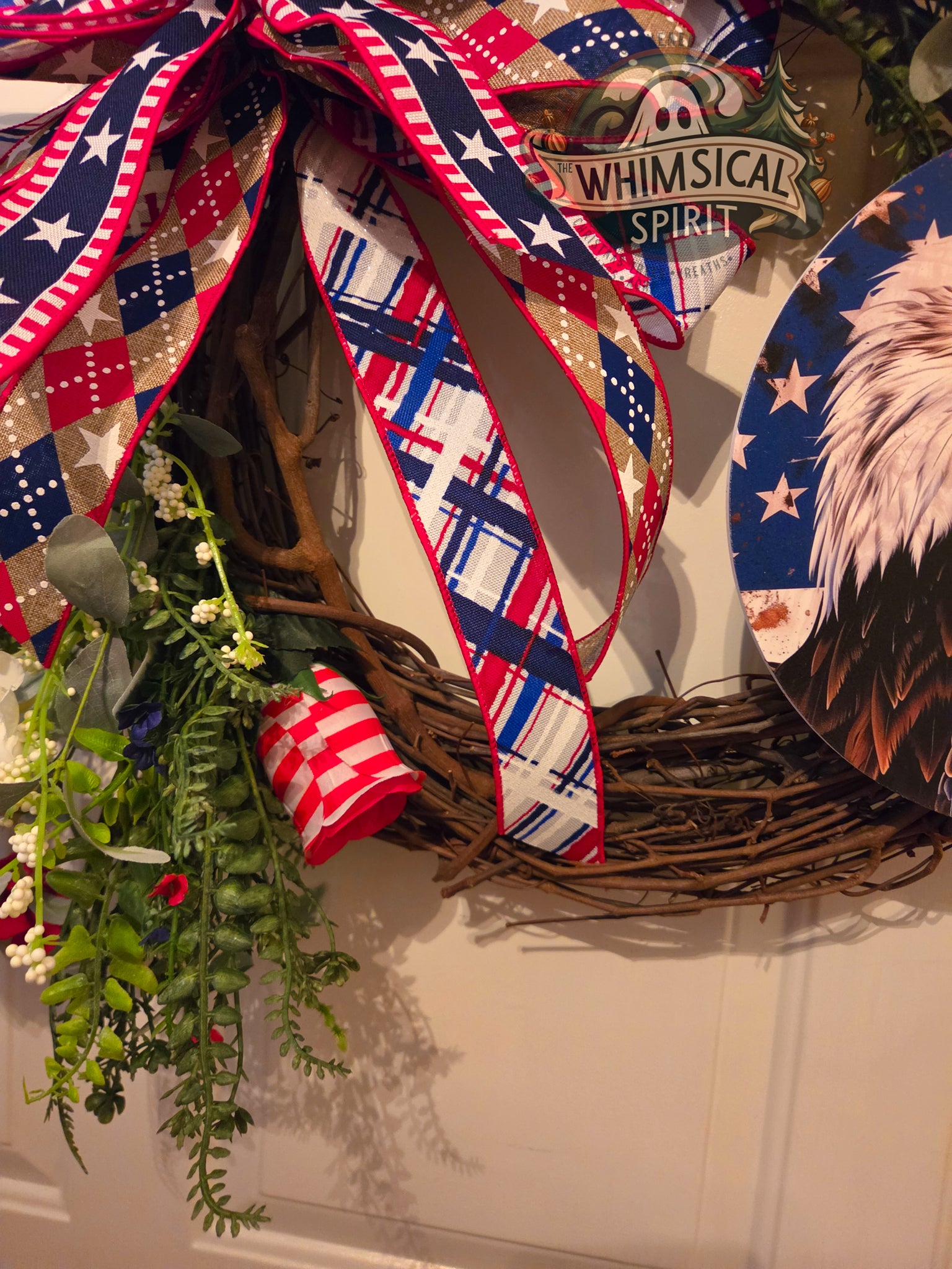 Decorative wreath with a large bow, eagle emblem, and 'Whimsical Spirit' sign on a white door.