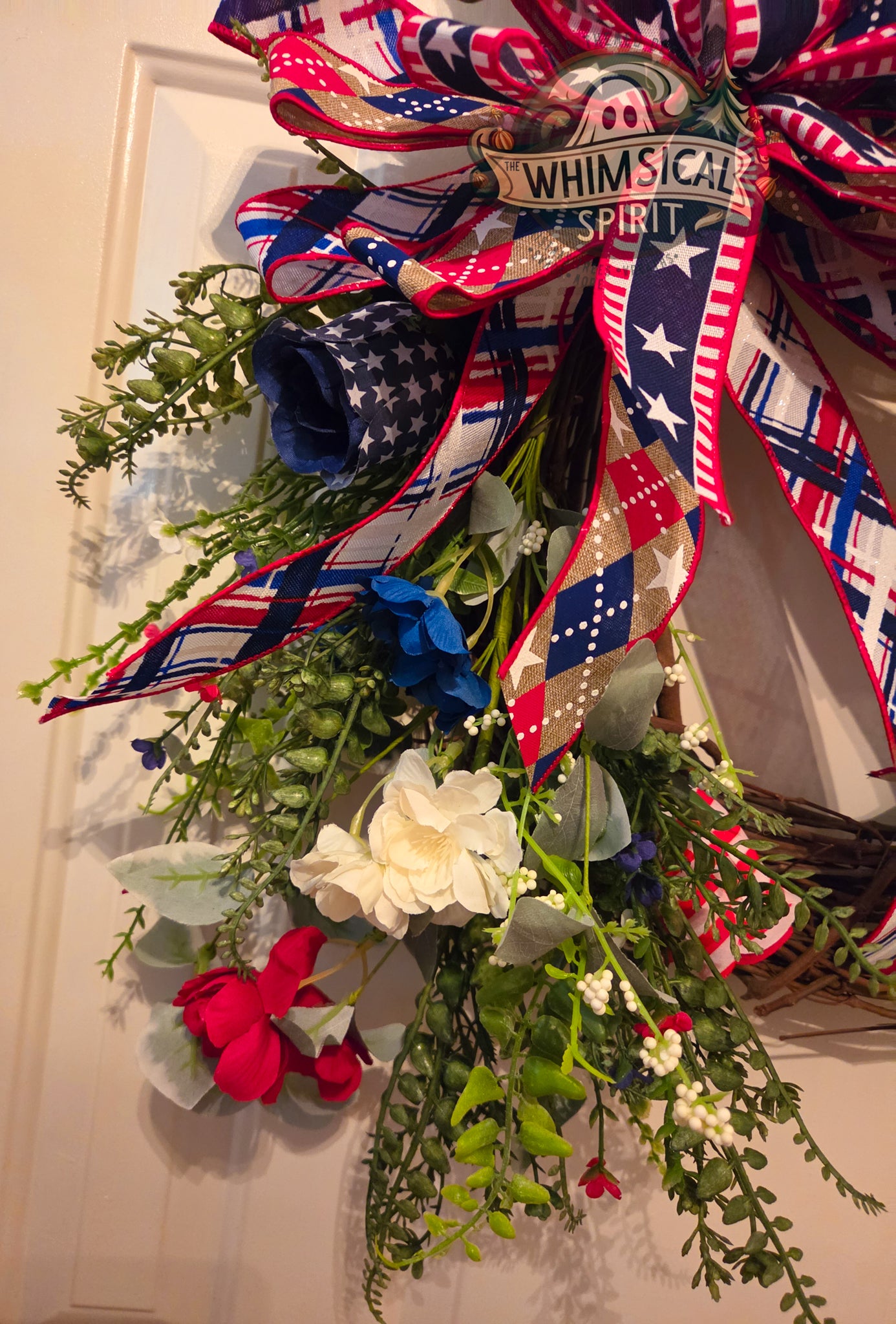 Decorative wreath with American flag colors and greenery on a door.