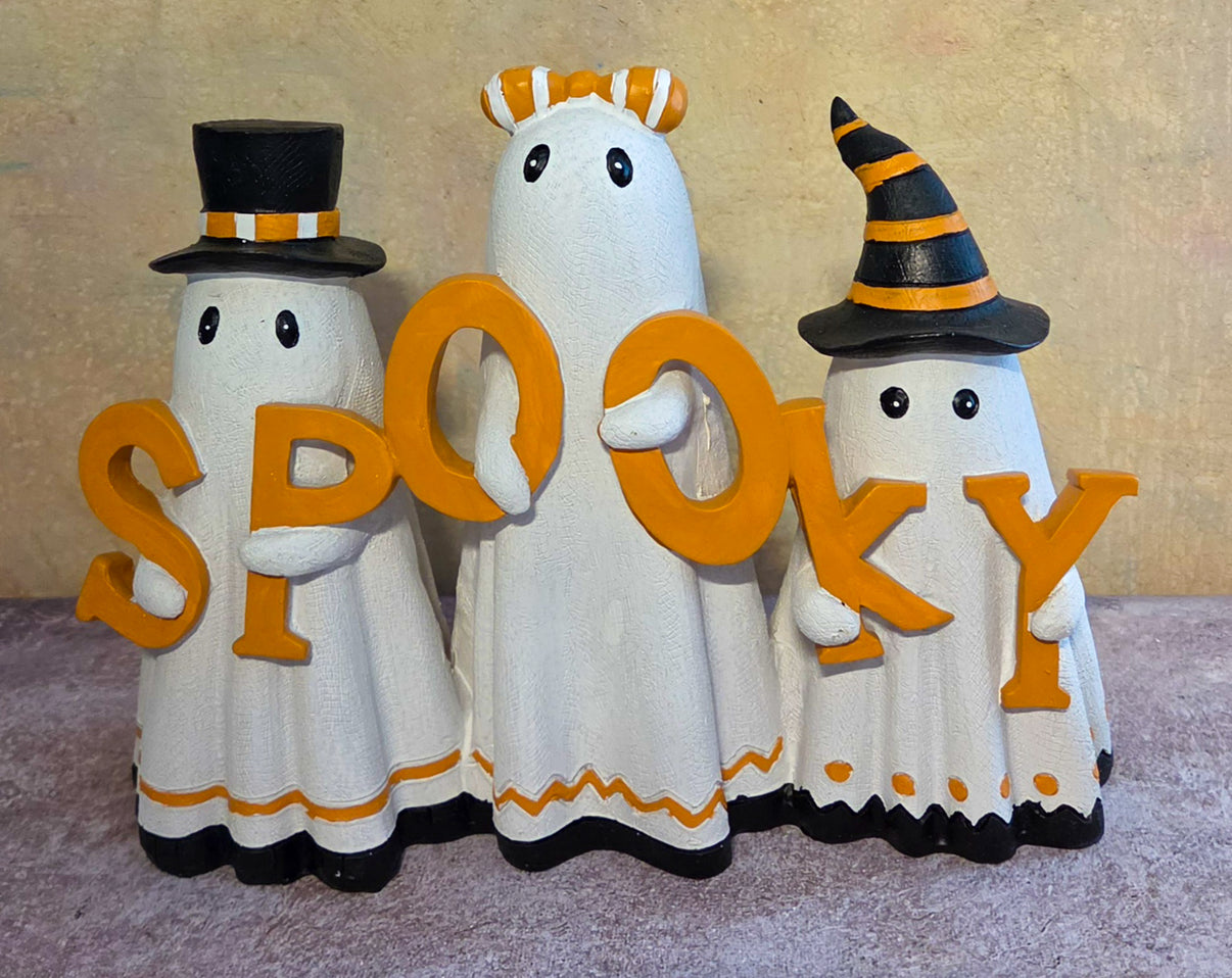 Front view of three white Halloween ghost figurines wearing festive hats and holding orange letters that spell SPOOKY.