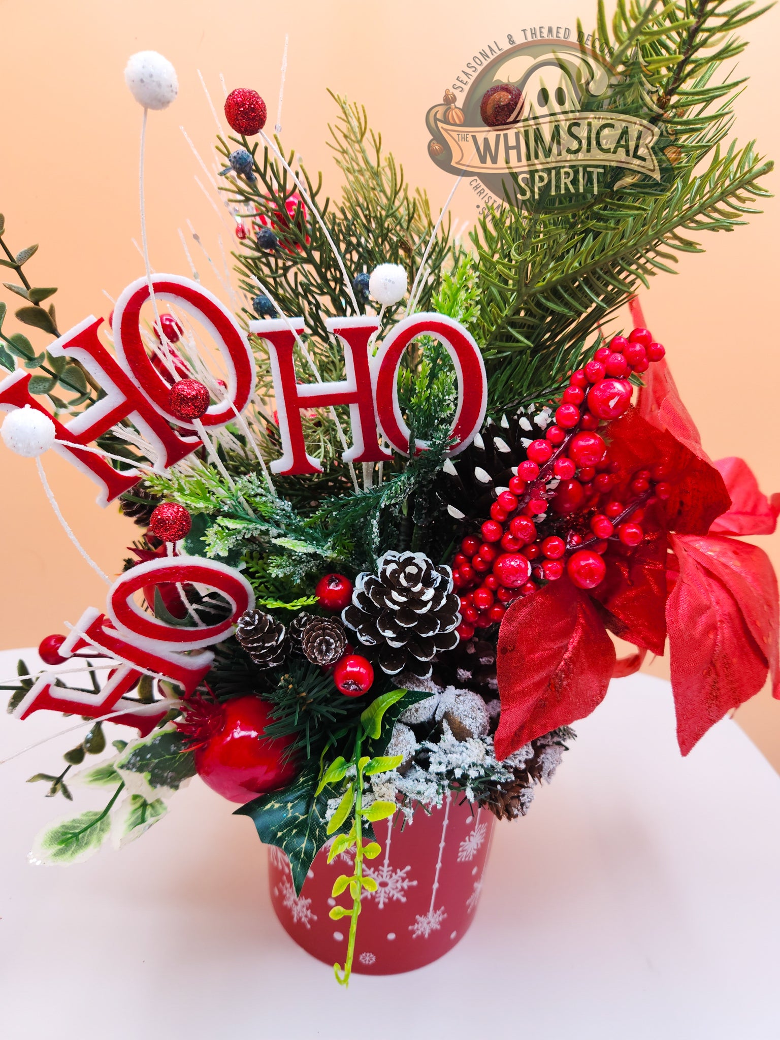 Decorative Christmas arrangement with 'HO HO' text, poinsettias, and pinecones on a beige background.