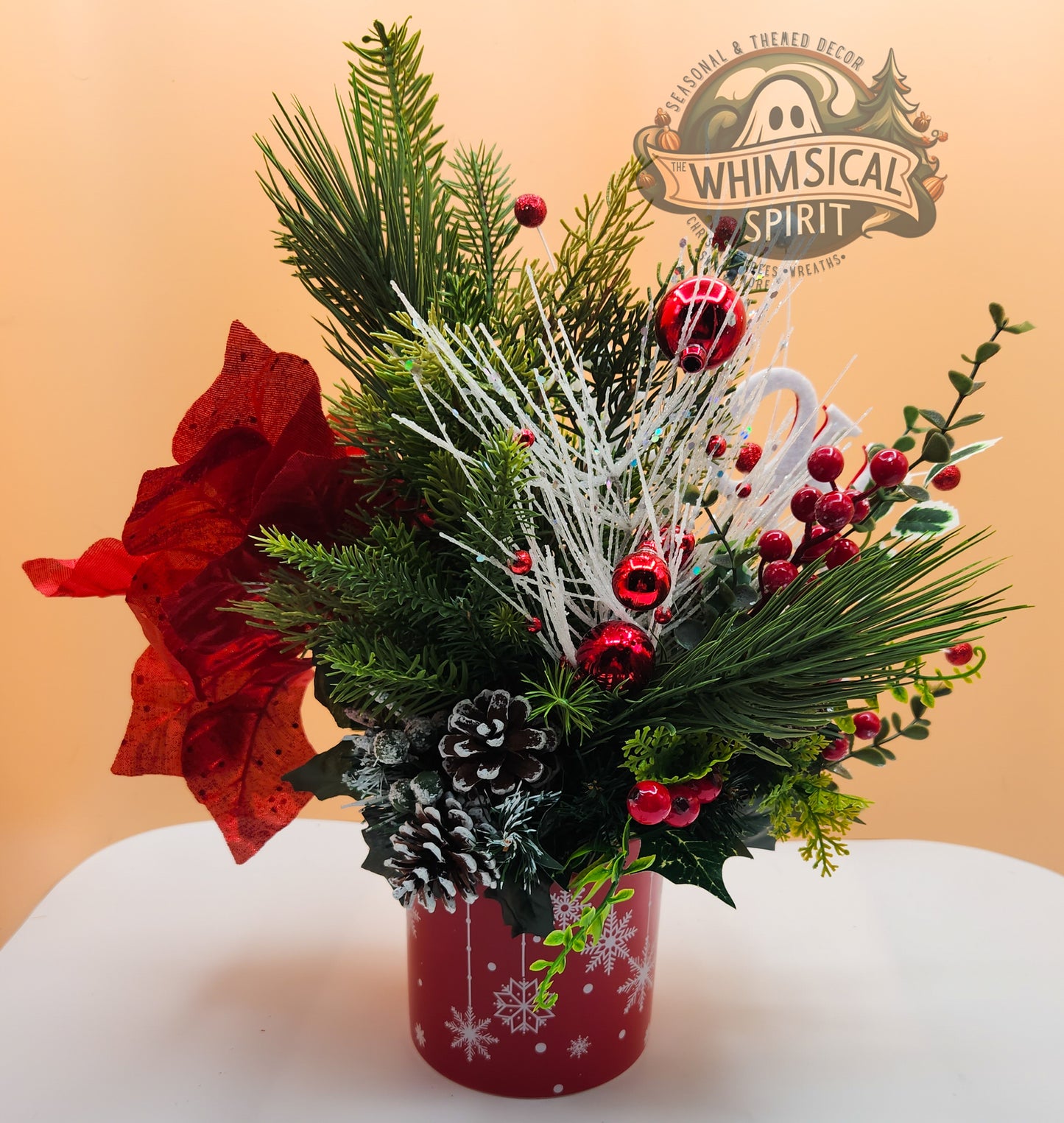 Christmas-themed floral arrangement with red and green elements on a white surface, featuring the 'Whimsical Spirit' brand.