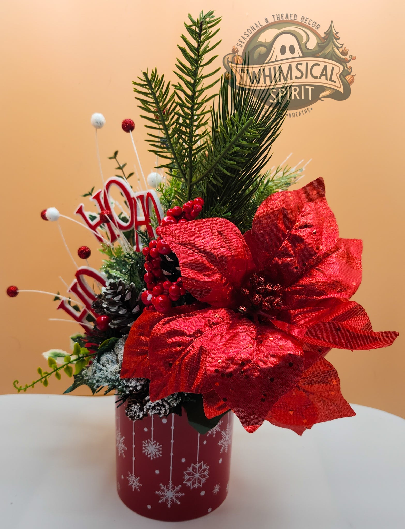 Christmas-themed floral arrangement with red poinsettias and greenery in a decorative vase, featuring the 'Whimsical Spirit' brand.