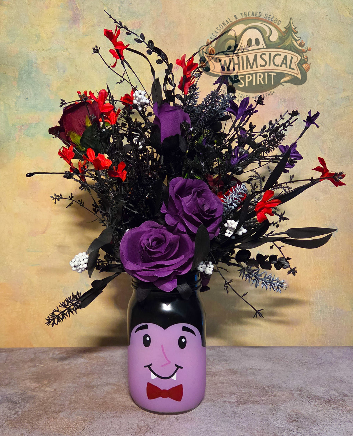 Full view of The Count’s Midnight Garden vampire vase centerpiece with purple roses, red blooms, and black foliage.