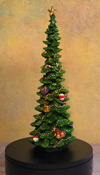Green decorated resin Christmas tree figurine with a gold star topper, gold garland, colorful ornaments, bells, and miniature gift accents.