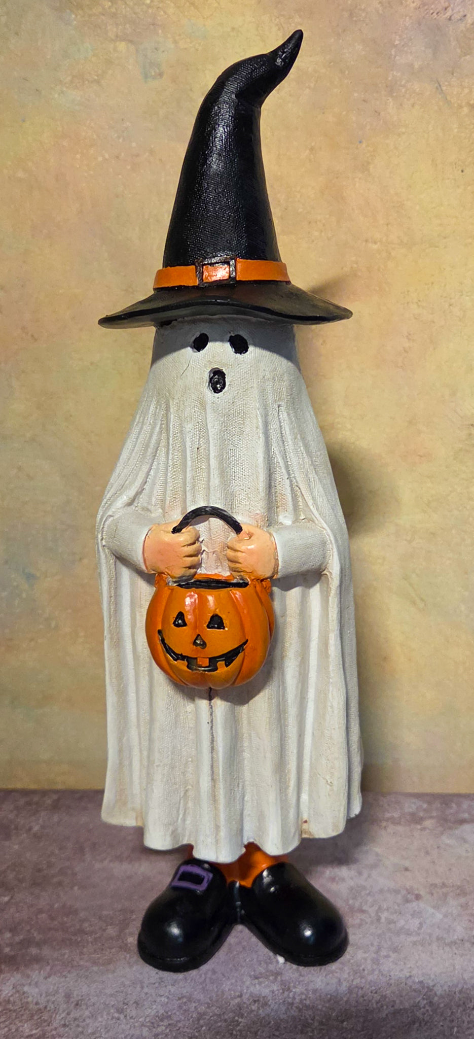 Tall Halloween ghost figurine wearing a pointed black witch hat and holding an orange jack-o’-lantern trick-or-treat bucket.