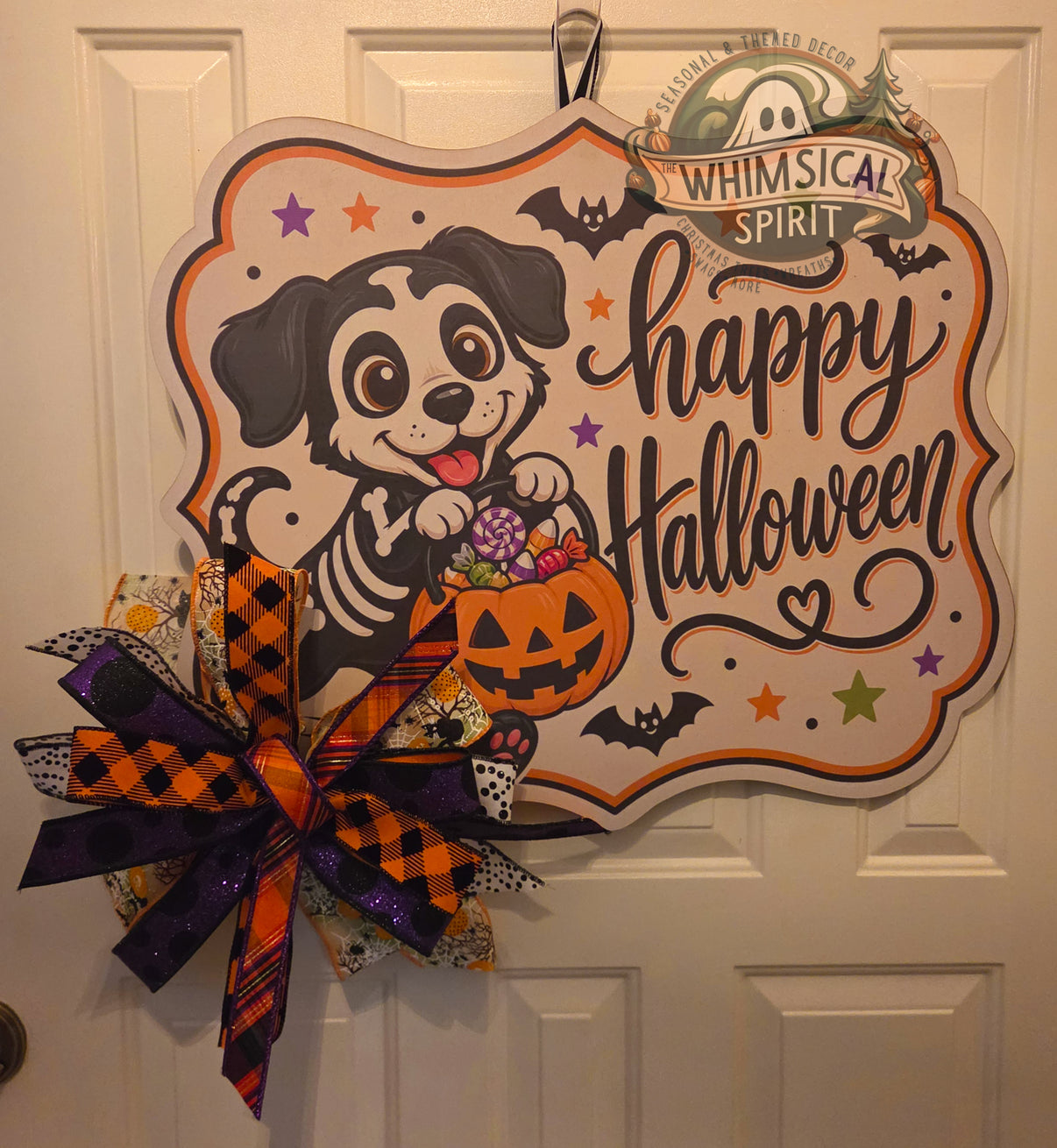 Tricks, Treats & Belly Rubs birch wood Halloween door hanger with a skeleton puppy, candy bucket, and large orange and purple bow
