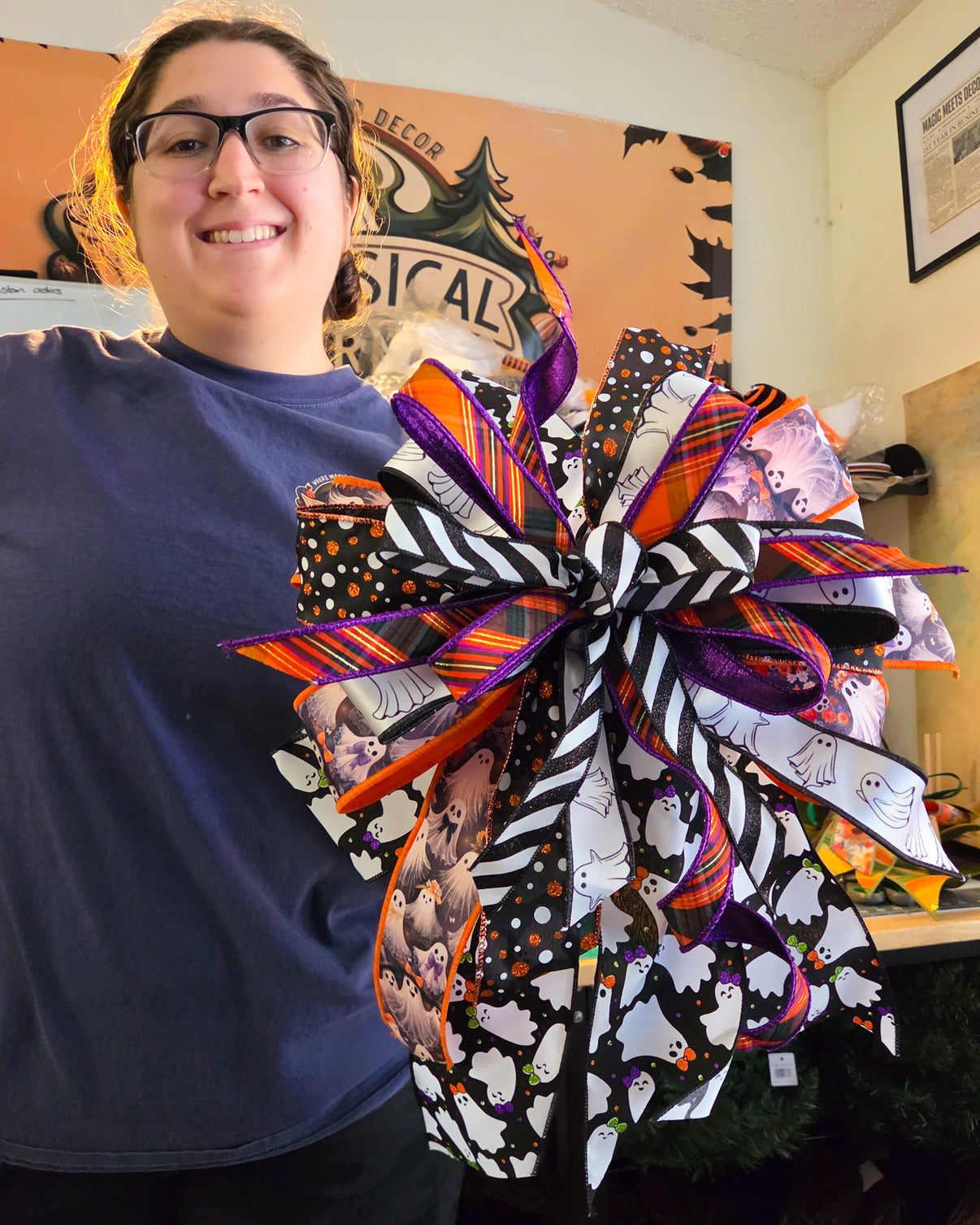 Maker holding an XL Halloween bow featuring layered purple, orange plaid, ghost, polka-dot, and black-and-white striped ribbon.