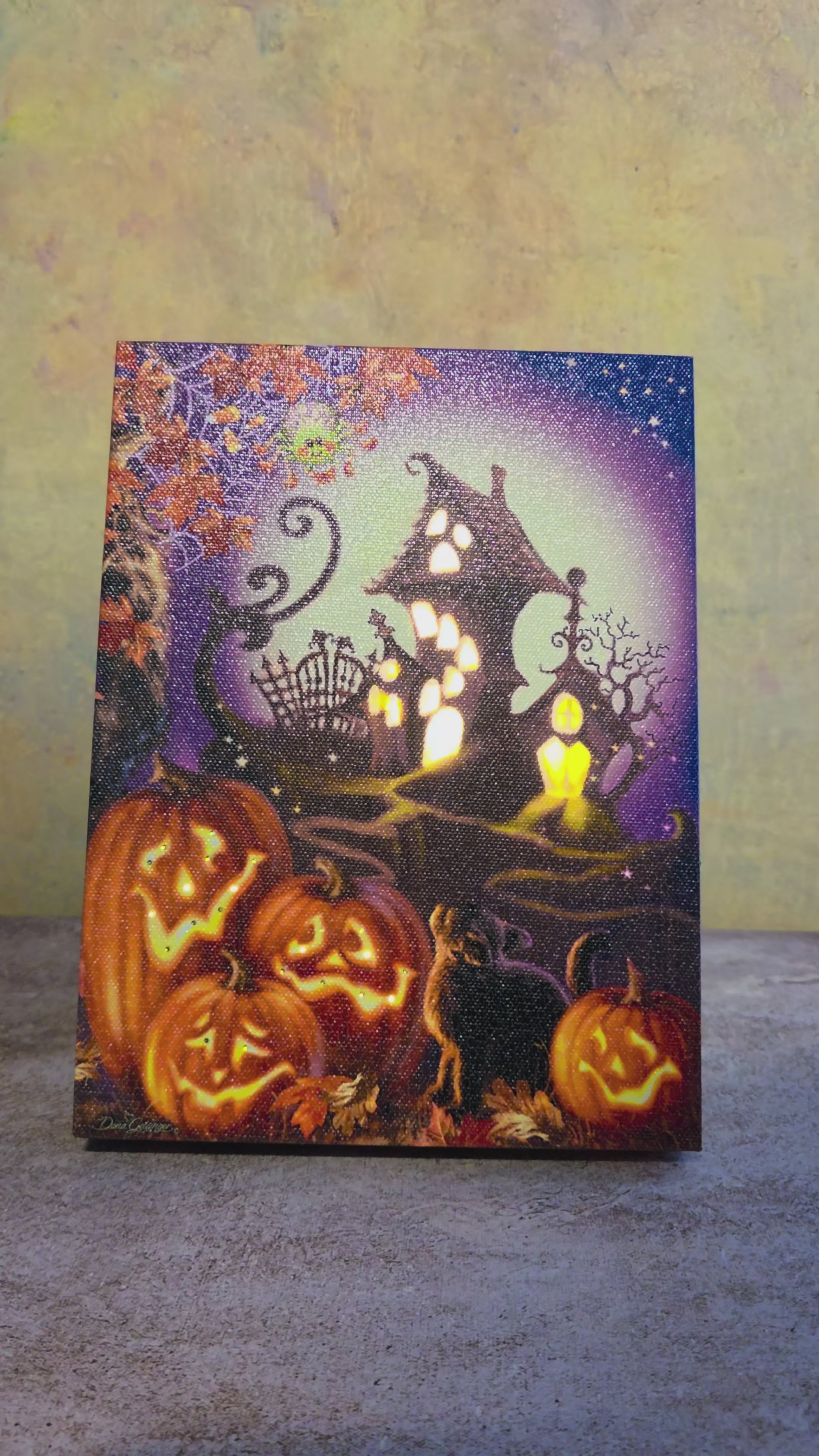 Video showing the light-up function on Haunted House, a Halloween tabletop canvas featuring glowing jack-o’-lanterns, a crooked haunted house, black cat, fall leaves, and a moonlit spooky scene.