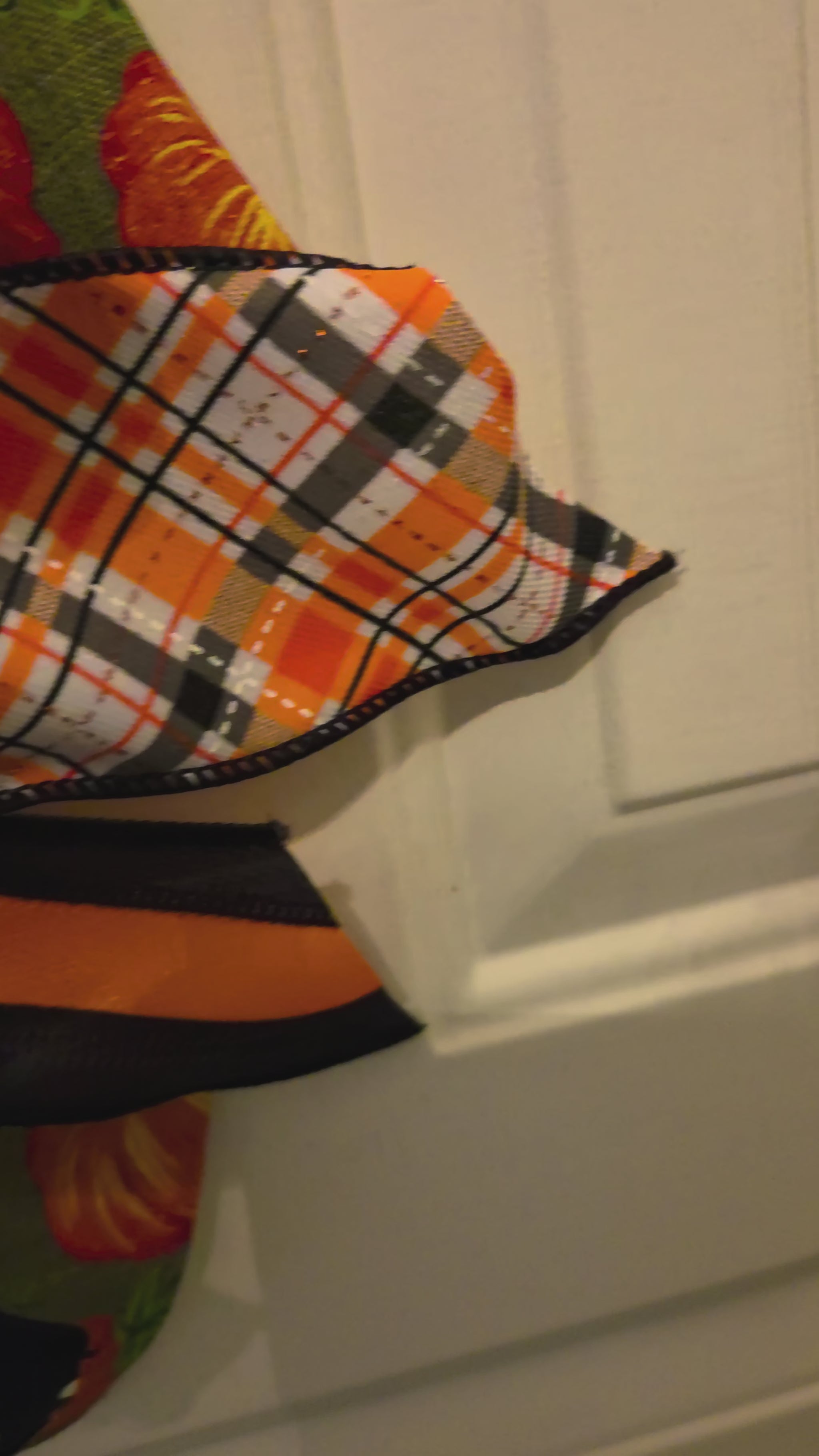Video showing a stacked fall pumpkin door hanger from multiple angles, highlighting the painted pumpkin design, black-and-white patterned details, leafy accents, and oversized seasonal bow.