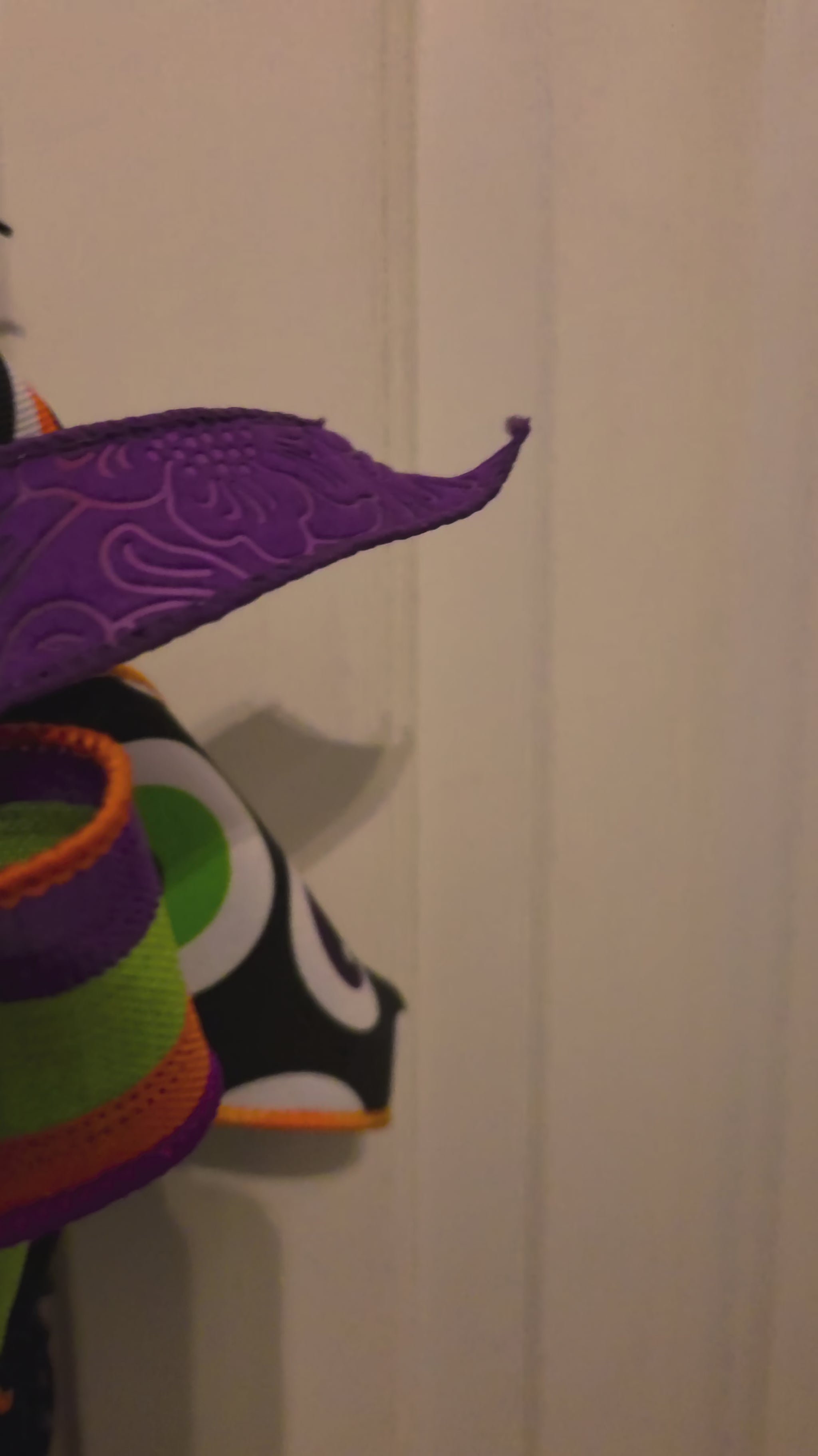 Video showing the grapevine witch legs Halloween door hanger from multiple angles, highlighting the purple curled boots, orange-and-black striped stockings, textured grapevine construction, and layered purple, green, orange, and black Halloween bow.