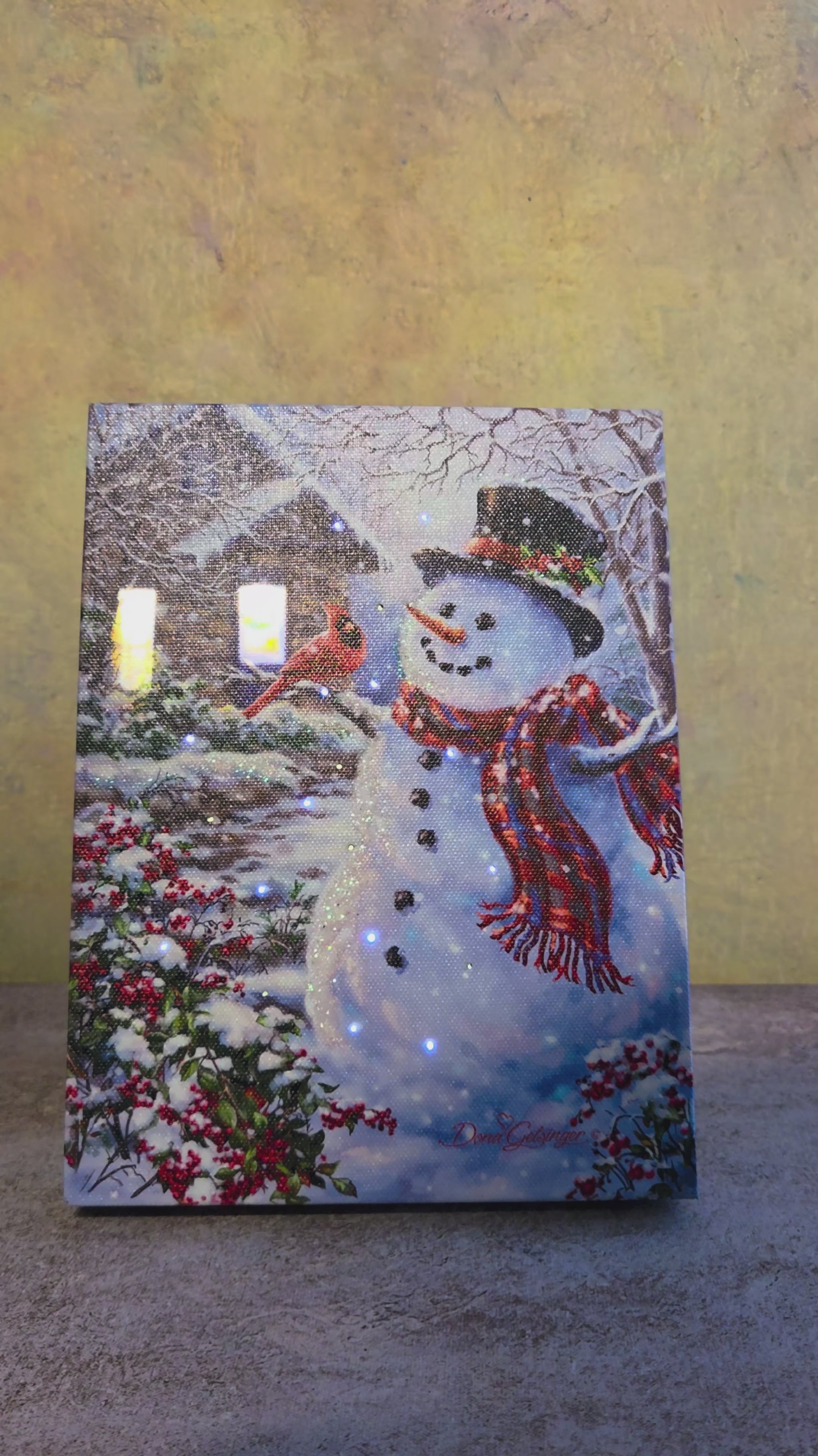 Video showing the light-up function on Snowman and Feathered Friend, a Christmas tabletop canvas featuring a smiling snowman, red cardinal, snowy cottage, red berries, and glowing winter details.