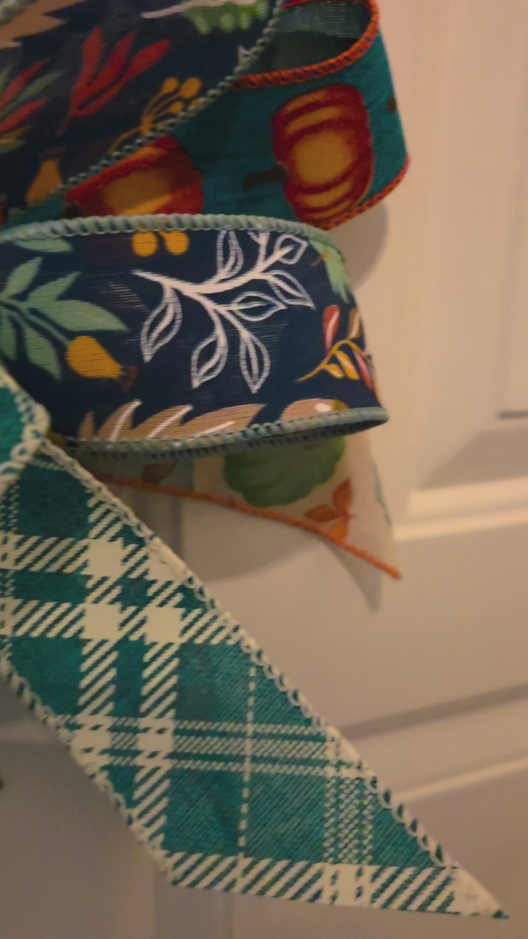 Video showing a stacked fall pumpkin door hanger from multiple angles, highlighting the navy and coral pumpkins, blue-and-white floral pumpkin, green leafy details, and layered teal and patterned bow.
